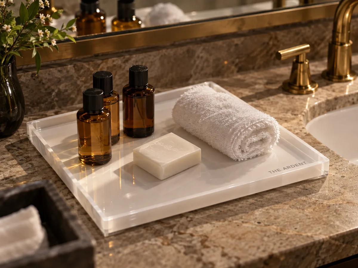 White acrylic amenity tray with an etched logo holding toiletries on a hotel bathroom vanity