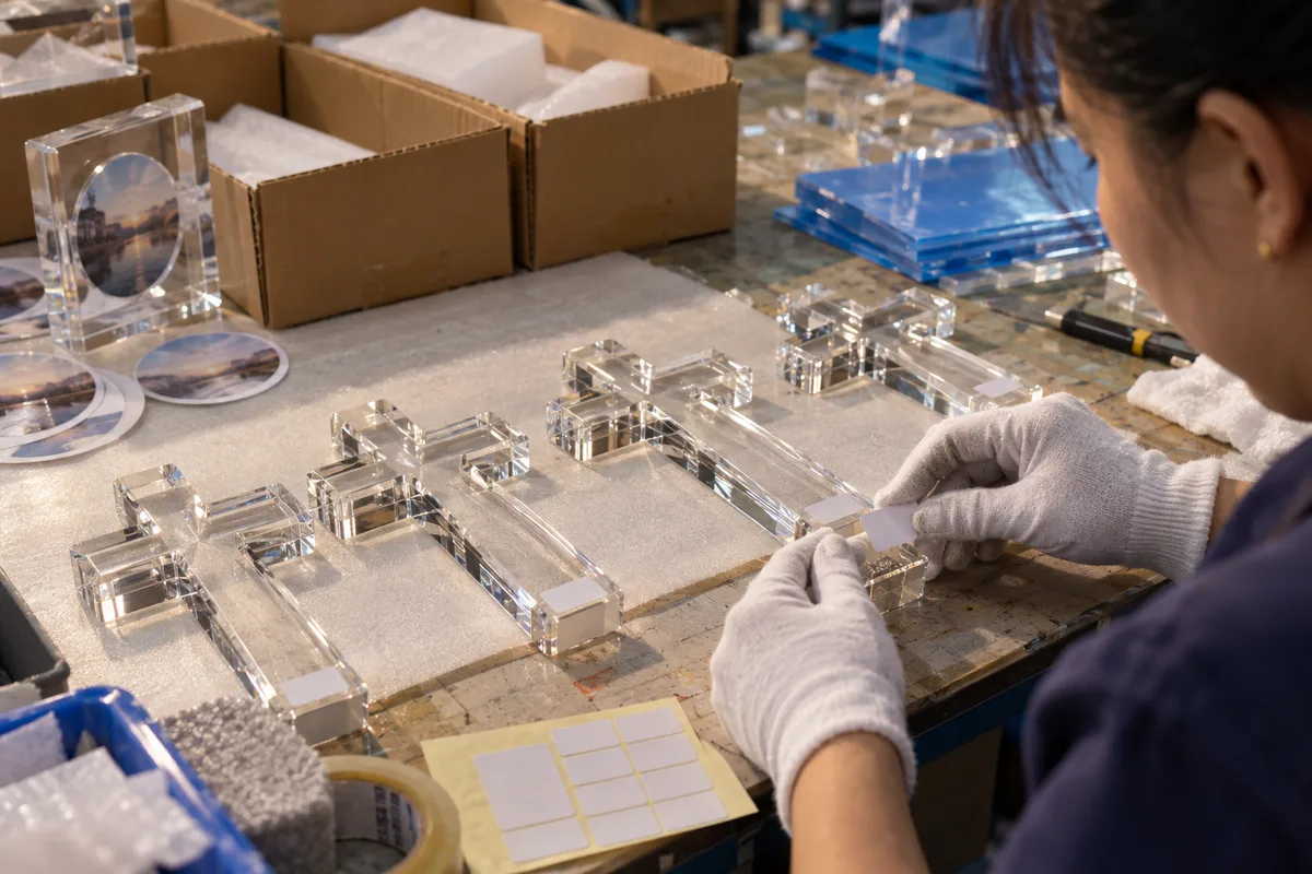 Applying base labels to clear acrylic cross shelf sitters before packing
