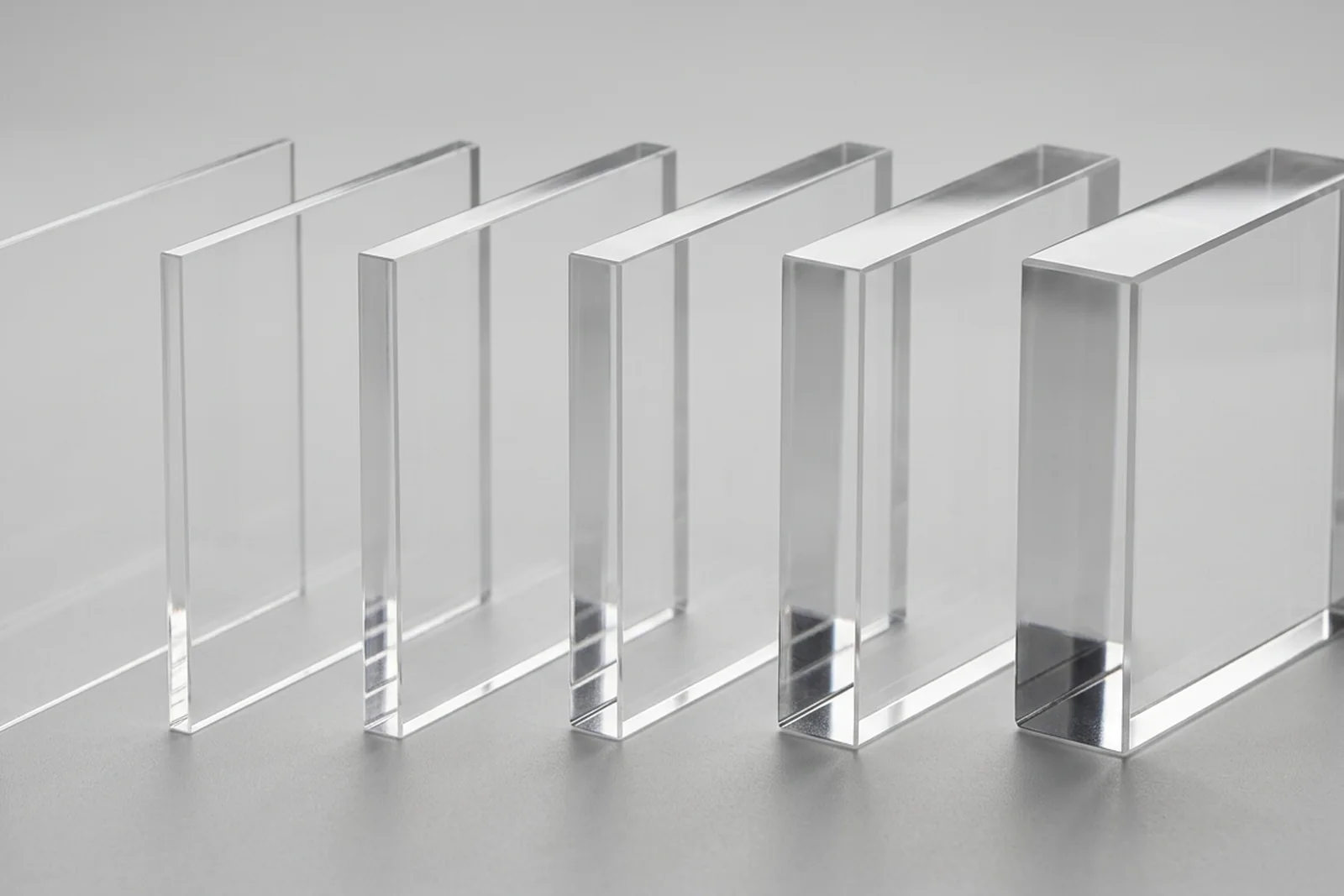 Six acrylic (PMMA plexiglass) sample squares stacked on edge from 3mm to 25mm, neutral gray background - thickness progression visible from paper-thin to heavy block.