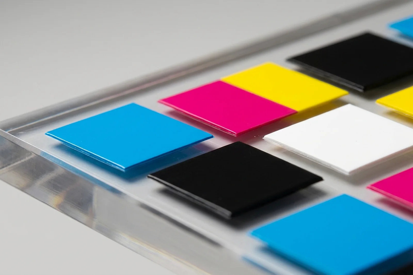 Macro close-up of a UV-printed CMYK color test block on a clear cast PMMA acrylic (plexiglass) sample - raised ink texture visible at high magnification, raking light reveals the cured surface finish.