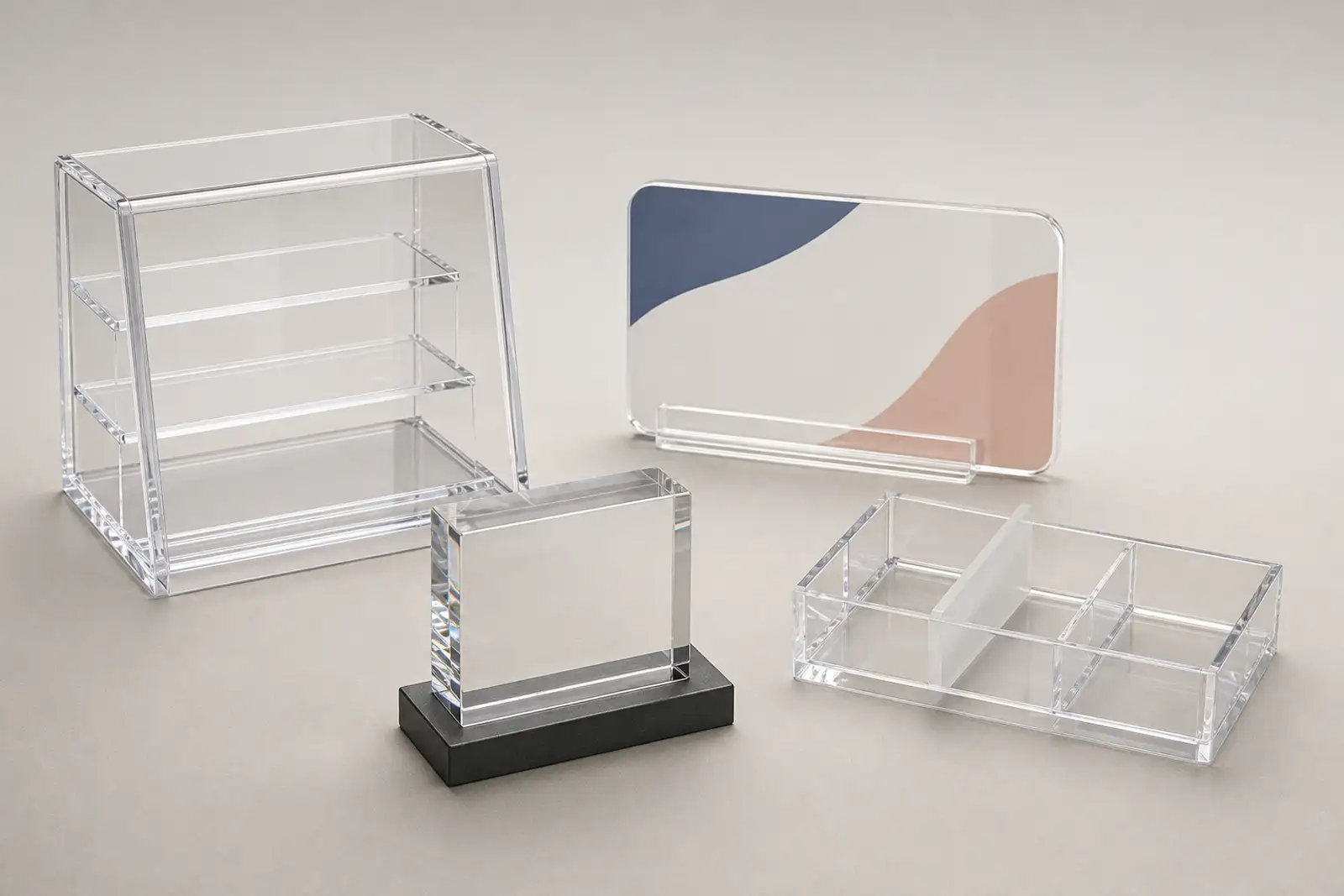 Range of finished custom acrylic fabrication products on a neutral studio surface — a clear acrylic POP display case, a UV-printed brand sign, a polished acrylic award block, and a cosmetics organizer with frosted dividers