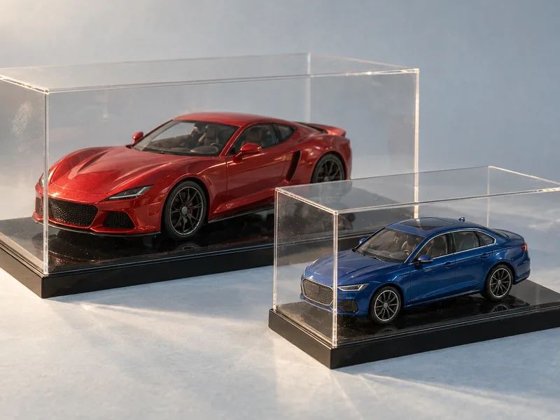 Two clear acrylic model car cases on glossy black bases holding a red 1:24 sports car and a blue 1:43 sedan