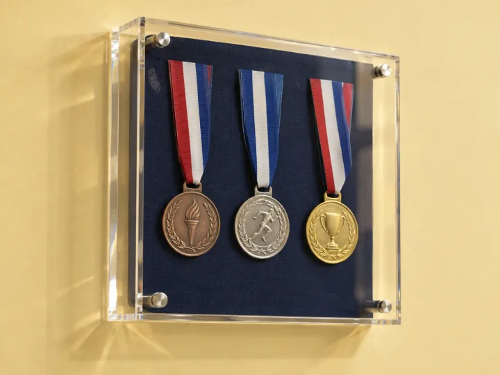إطار صندوقي (Shadow Box) شفاف من الأكريليك مثبّت على الحائط يحمل ثلاث ميداليات على خلفية كحلية