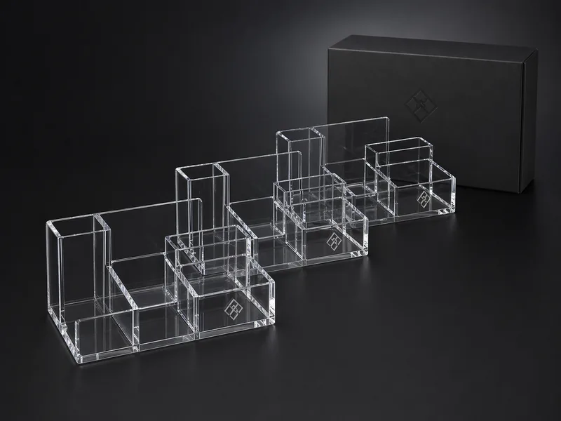Three matching clear acrylic corporate desk caddies with a boxed program sample on a dark backdrop