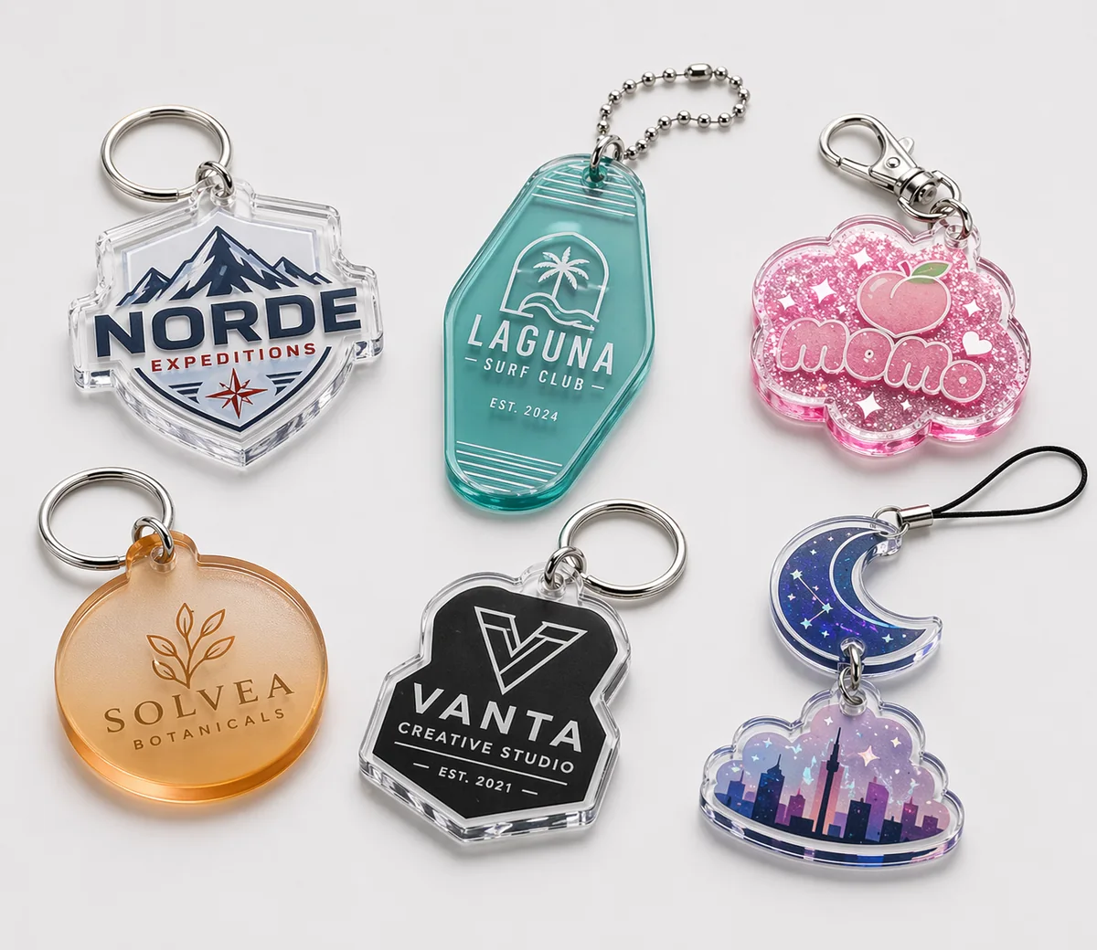 Collection of custom acrylic keychains showing clear, colored, glitter, frosted, opaque, and multi-piece styles with mixed attachment hardware