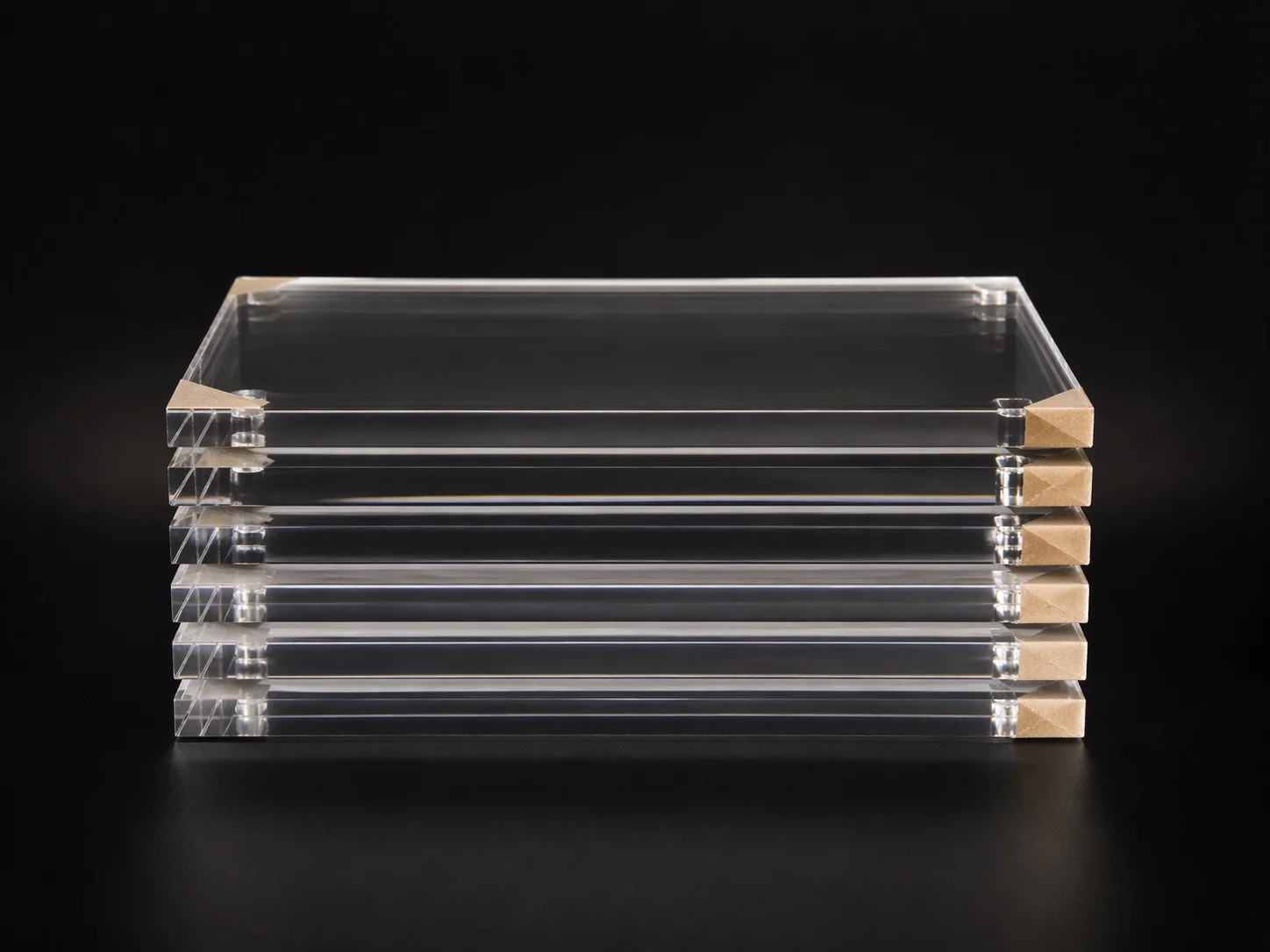 Stack of blank 5 by 7 acrylic photo blocks with protective film corner tabs on a dark studio background