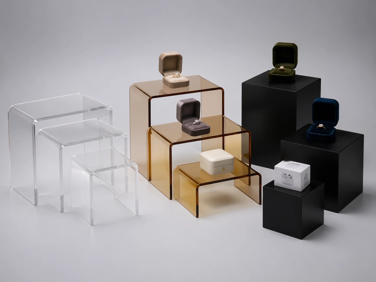 Clear nesting acrylic risers, amber U-shaped risers, and black pedestal risers arranged for retail display comparison