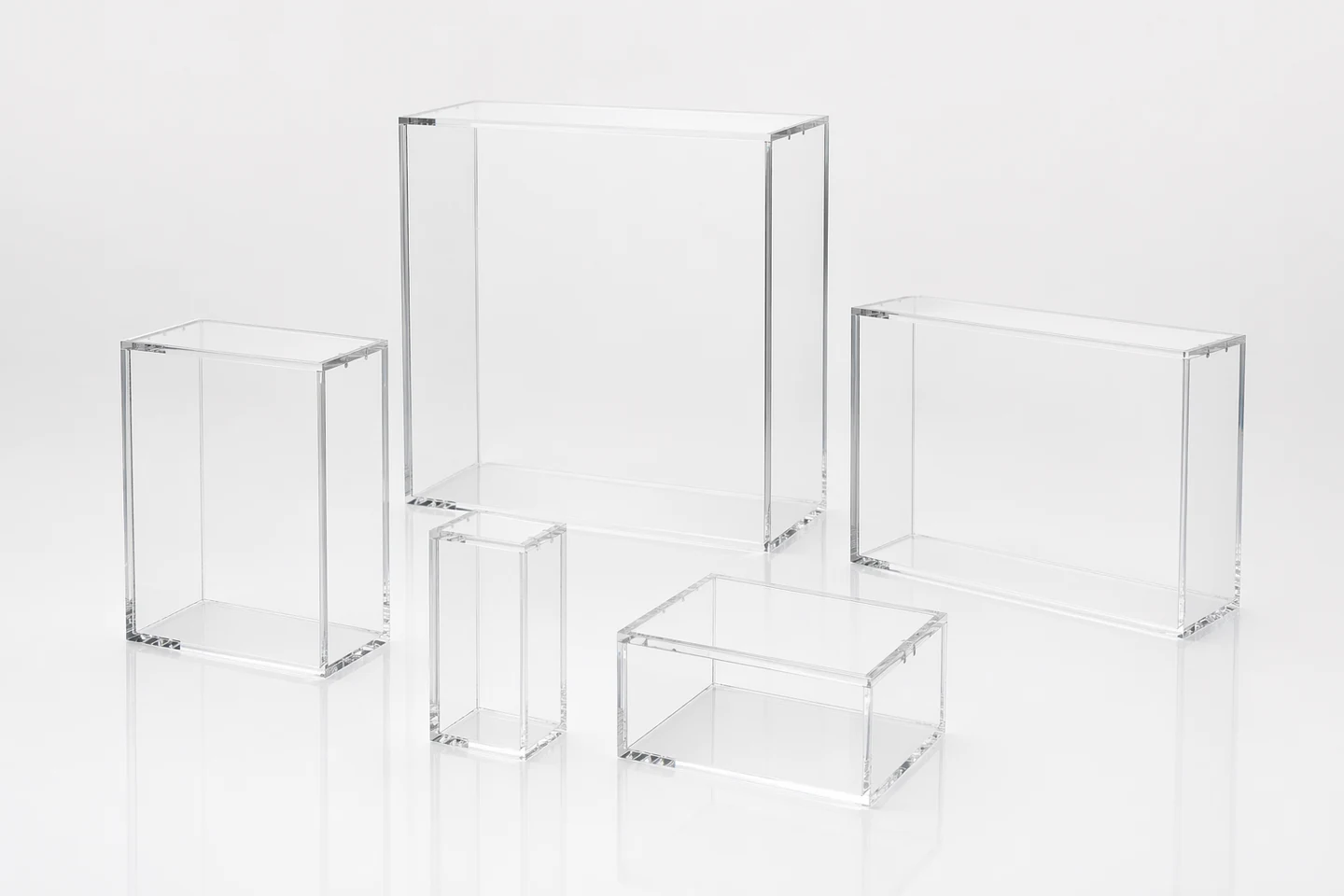 Family lineup of five empty clear acrylic TCG display cases in different booster box, ETB, UPC, and Japanese card box sizes