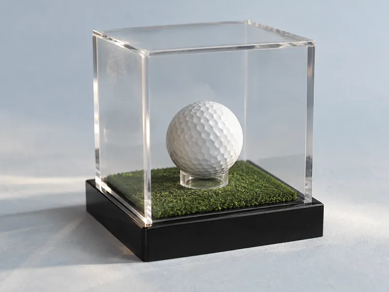Golf ball on a tee under a clear acrylic cover on a black acrylic base