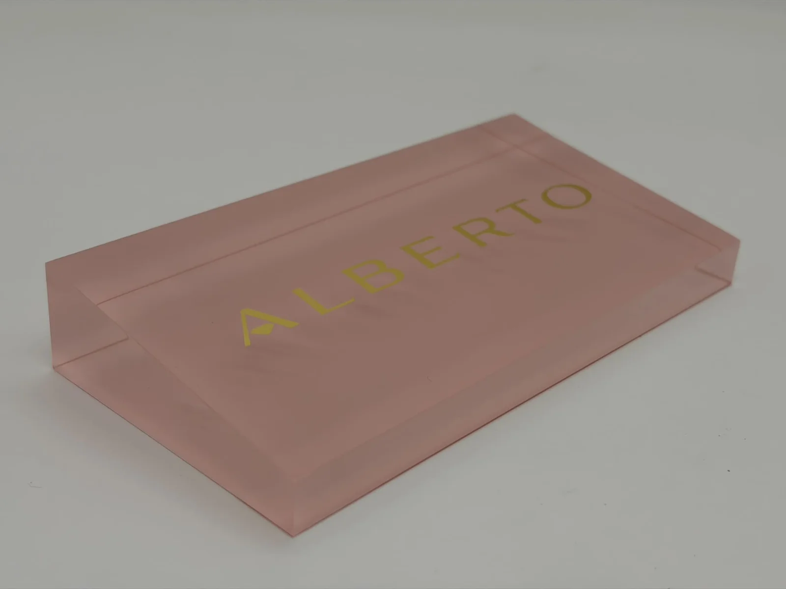 Pink tinted acrylic logo block with gold lettering and polished bevels