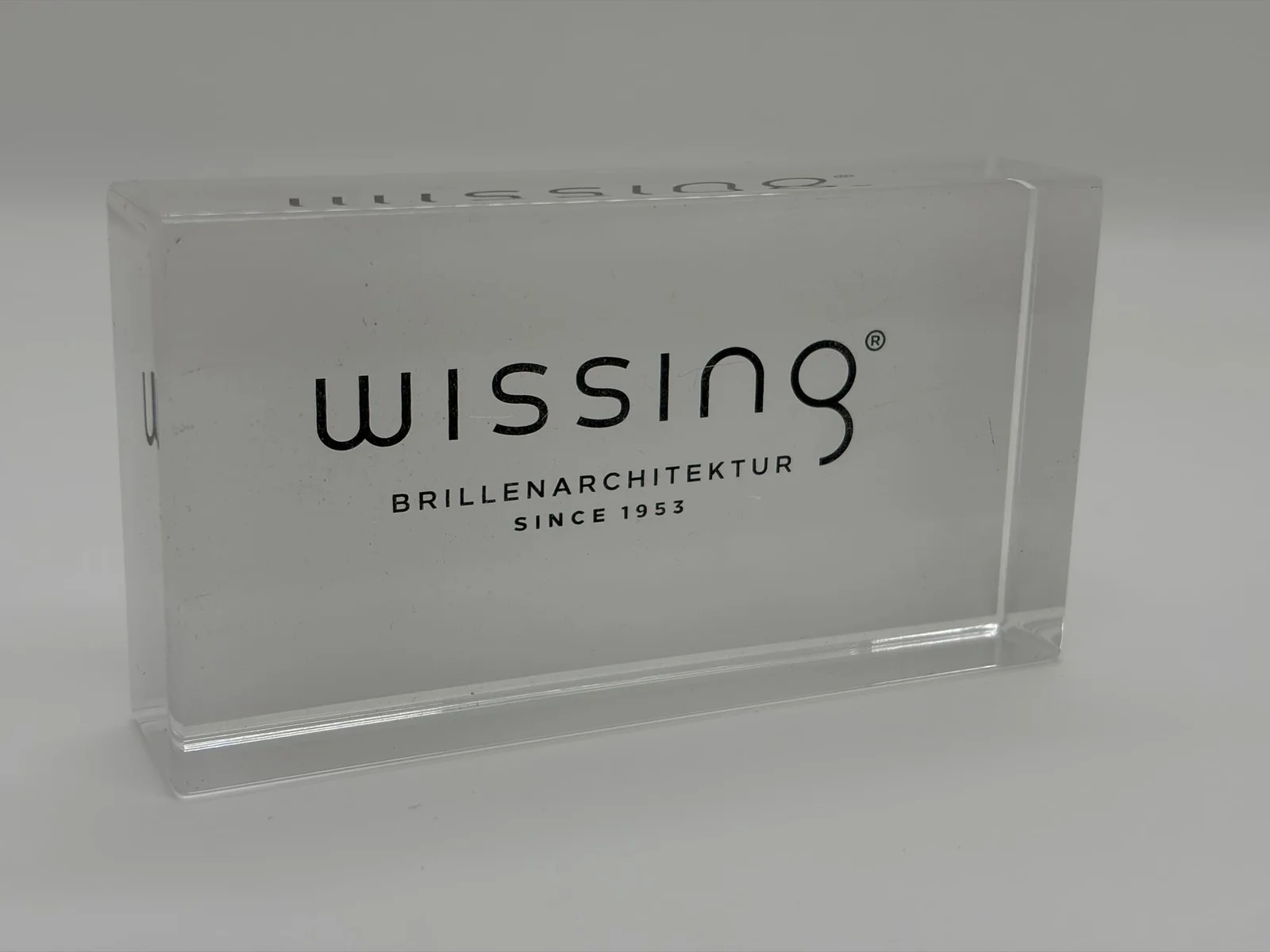 Clear acrylic logo block with black reverse-printed branding viewed through the polished acrylic thickness