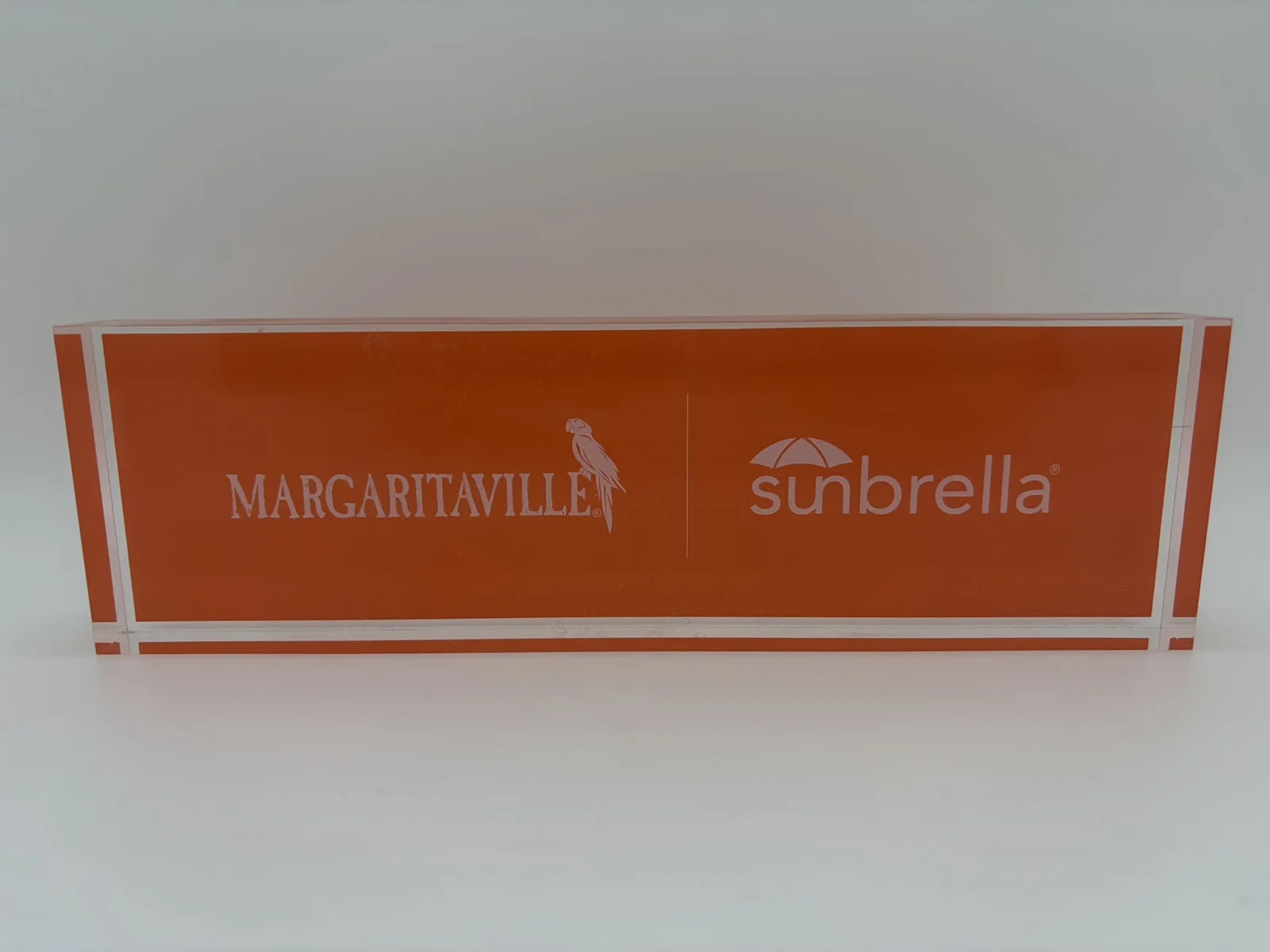 Long orange co-branded acrylic logo block with white logos behind clear acrylic